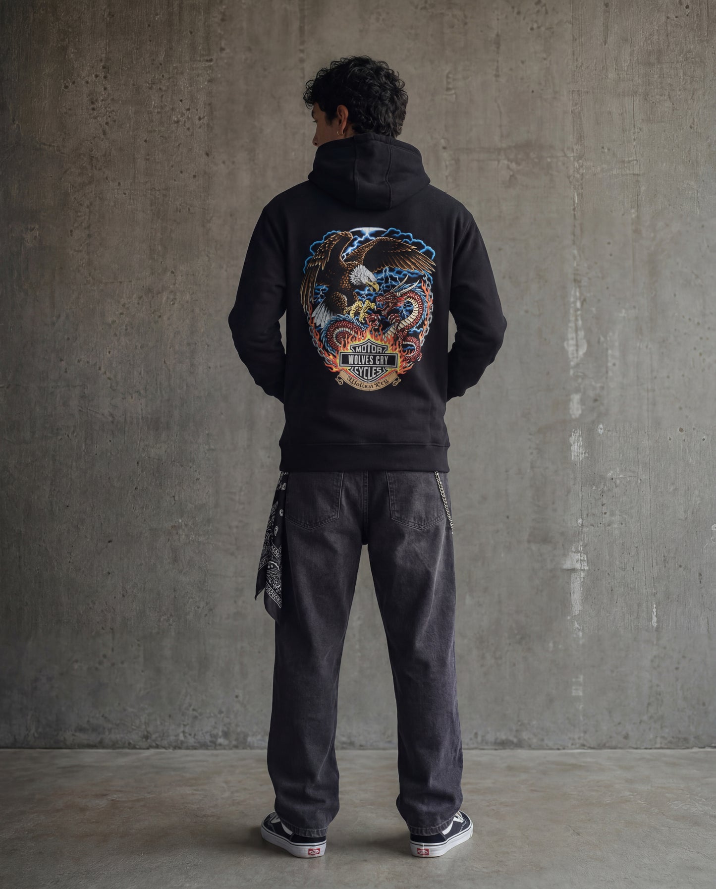 Person wearing a black hoodie with a colorful graphic on the back against a concrete wall.