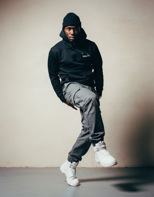 Model wearing a black wolves cry originals hoodie against a neutral wall- representing strength, confidence, and everyday armour 