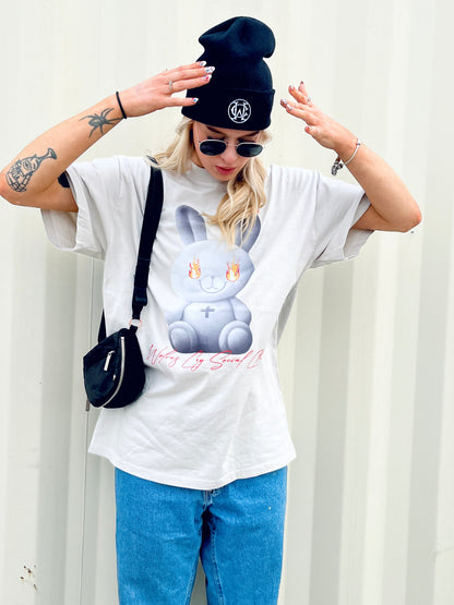 Model wearing the Wolves Cry Oversized Teddy Tee in bone off-white, featuring a graphic of a teddy engulfed in flames, styled with a black beanie and sunglasses.