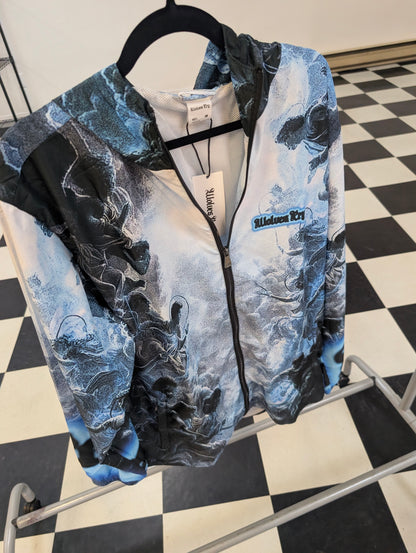 A Wolves Cry zip-up jacket with a blue and black abstract print, hanging on a black hanger on a clothing rack over a black and white checkered floor.