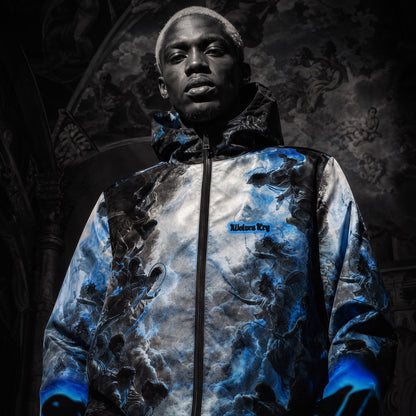 Wolves cry outerwear collection of A man wearing a Wolves Cry hooded Windbreaker jacket with a dramatic blue, gray, and black abstract print, posed against a dark, ornate interior background. The jacket has a small blue 'Wolves cry' logo on the left chest.