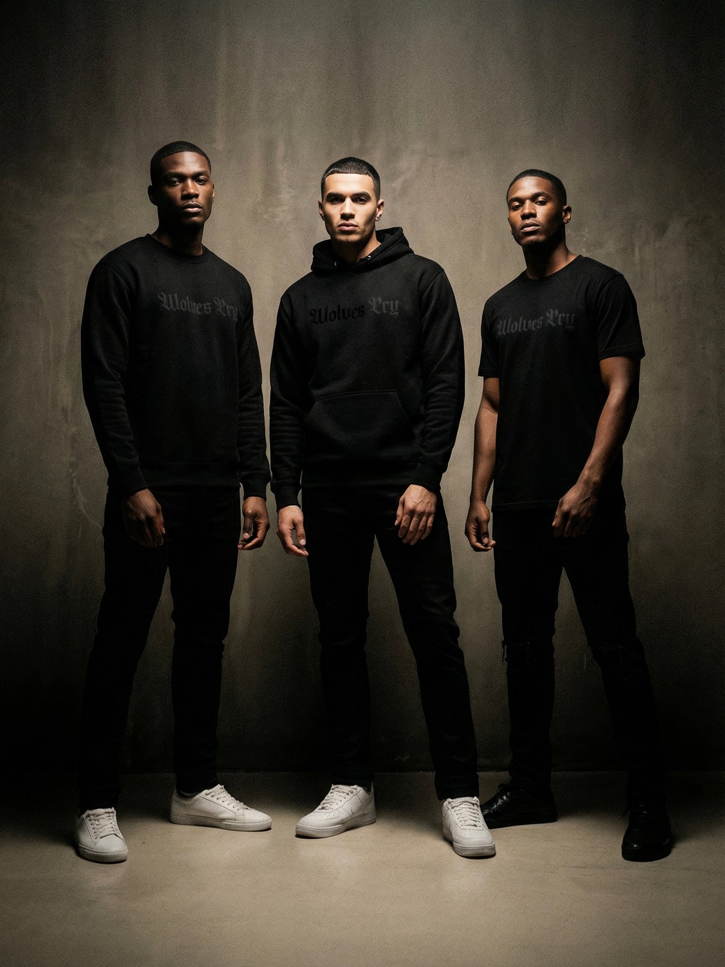 Three men wearing black hoodies and pants standing against a gray background