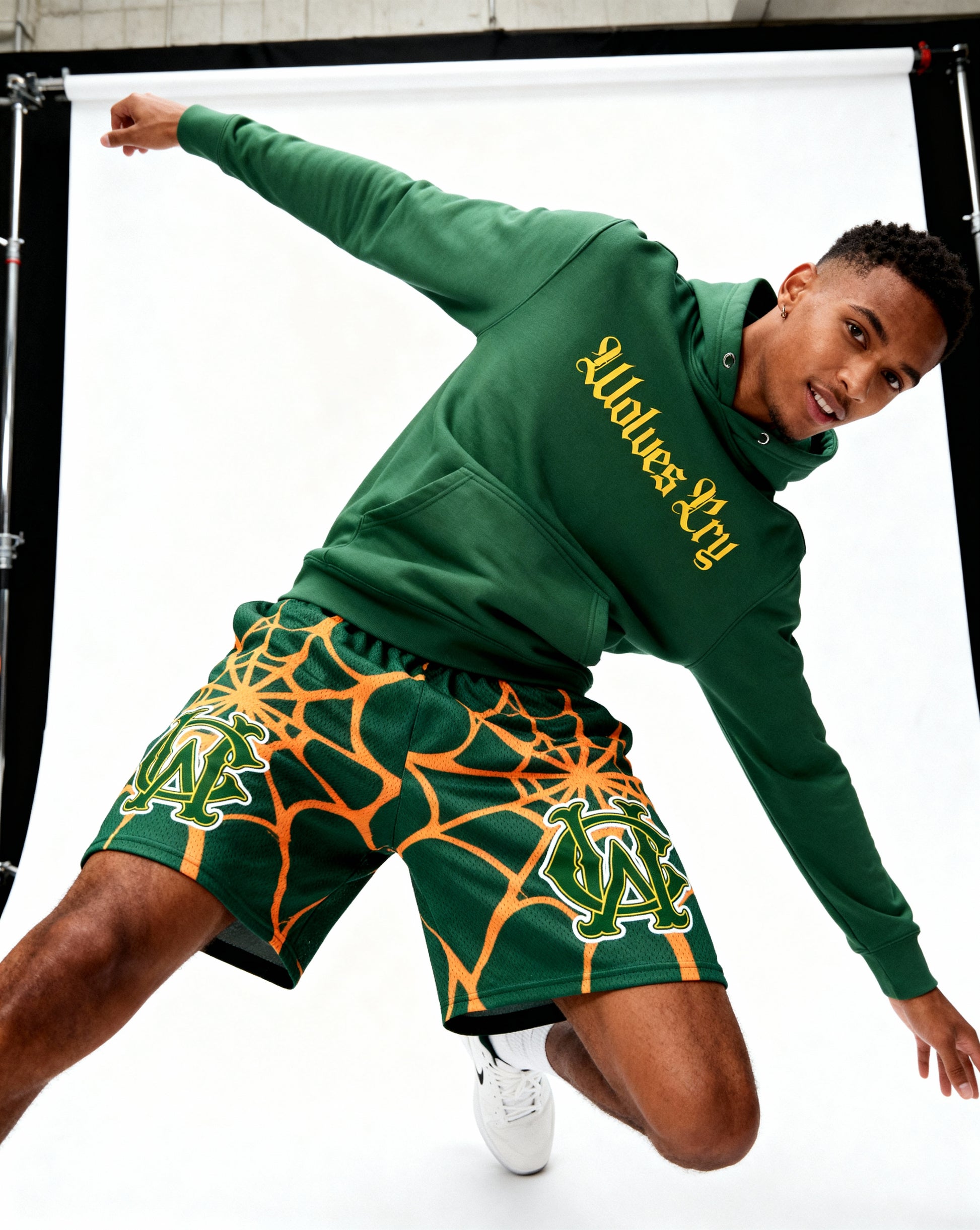 Model wearing Wolves Cry Everyday Spellout Hoodie in forest green and yellow — high-energy streetwear look capturing vintage athletic heritage and modern edge.