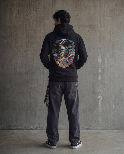 Person wearing a black hoodie with a colorful graphic on the back against a concrete wall.