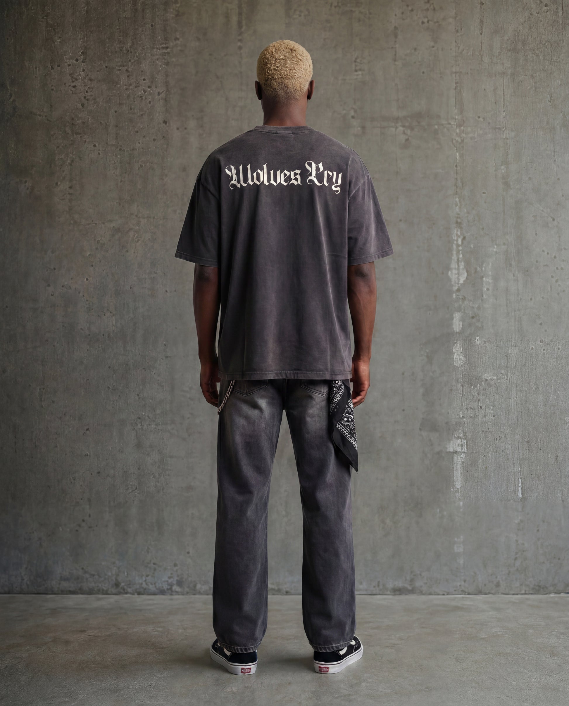 Person wearing a Wolves Cry dark gray t-shirt with 'Wolves Cry text, standing against a textured gray wall.