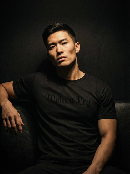 Man wearing a black t-shirt with 'Wolves Cry' text, sitting against a dark background
