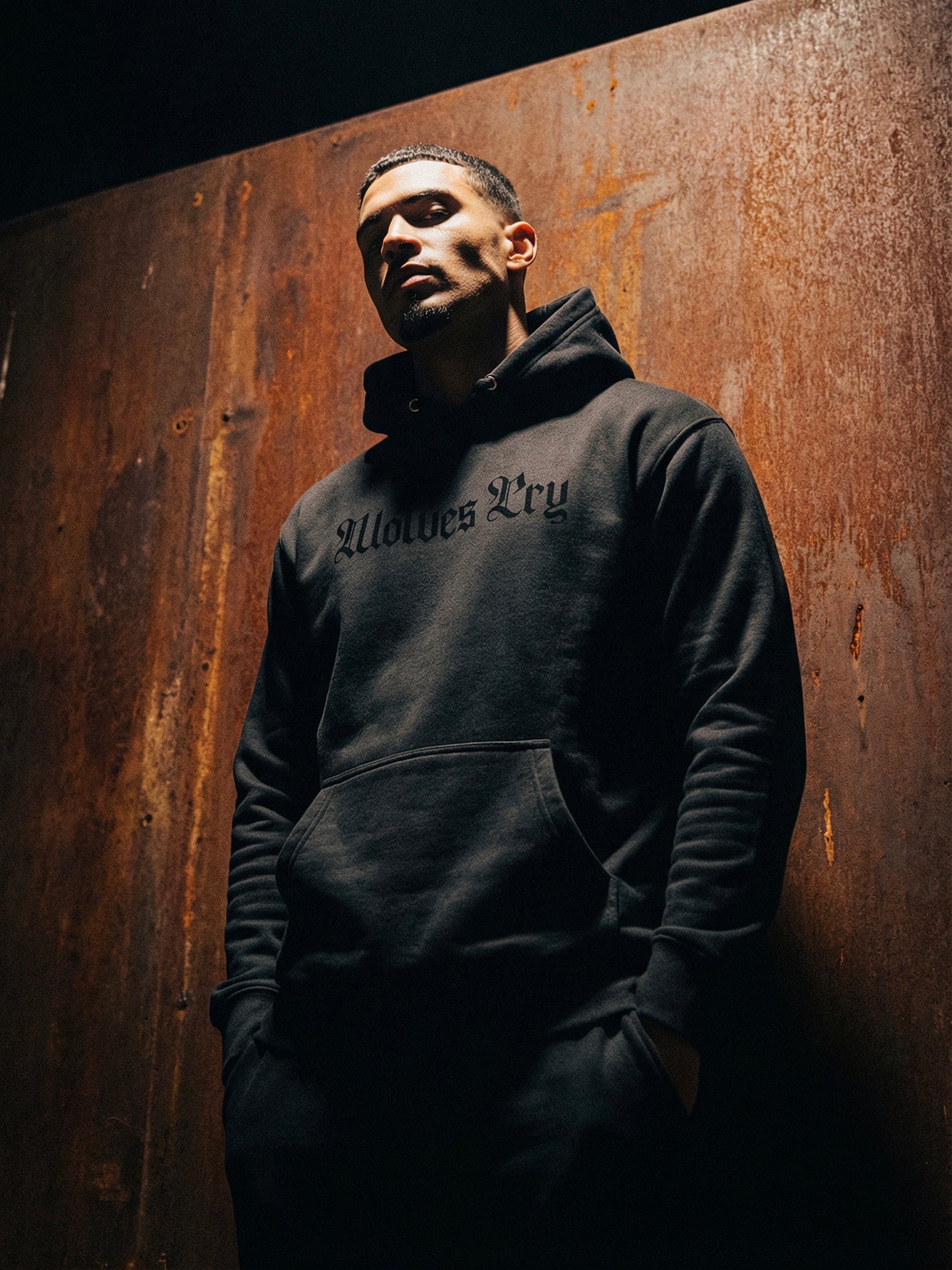 Person wearing a dark hoodie with text against a textured brown wall