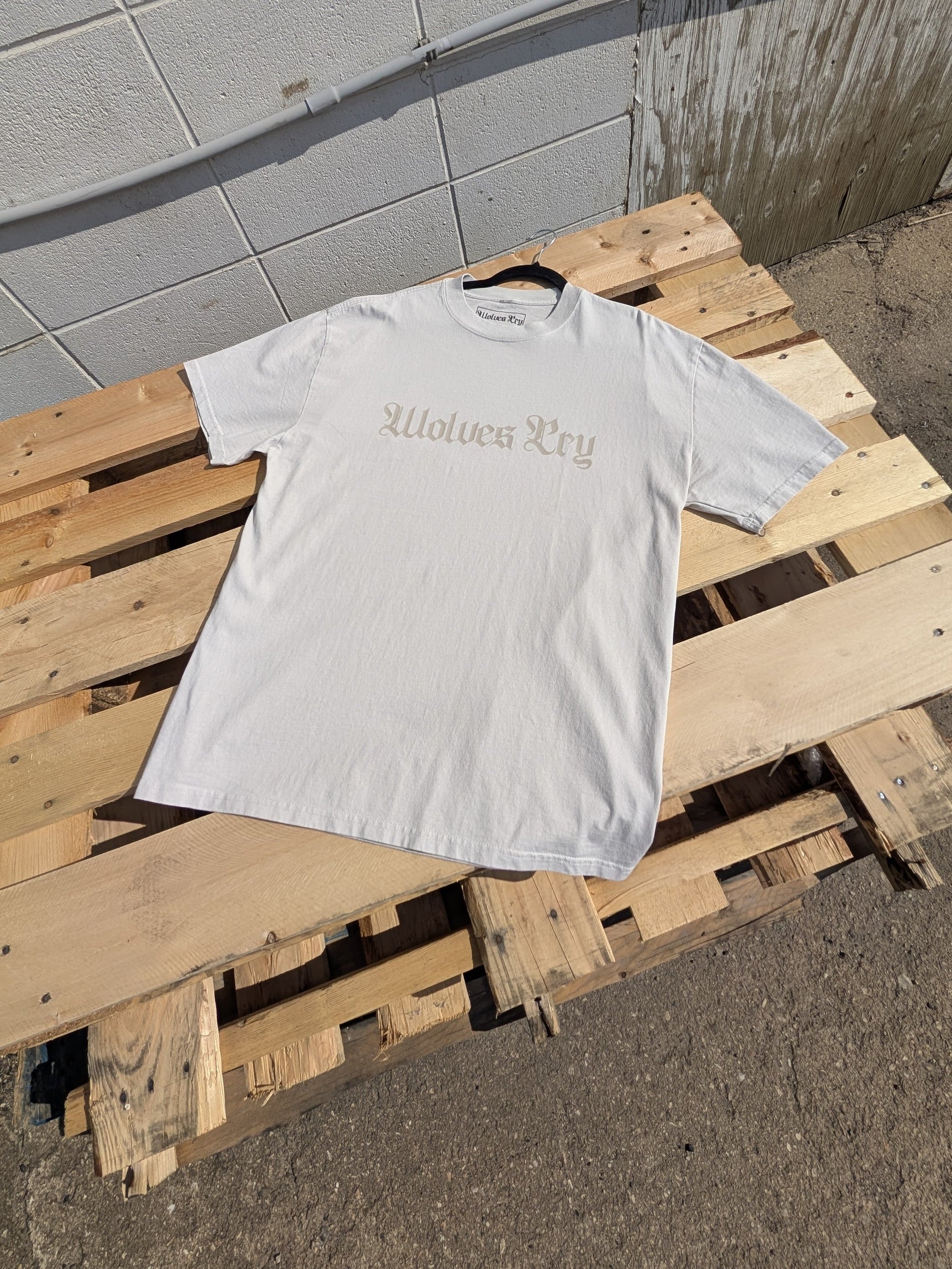 Flat lay of Wolves Cry Oversized Bone Tee with faded off-white spell-out graphic — neutral tone-on-tone tee with subtle, refined street identity.
