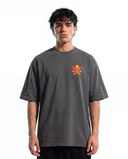 A man wearing a washed charcoal gray t-shirt with a small red and yellow graphic on the left chest, photographed against a solid white background.